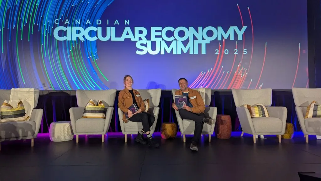 Two people seated on stage at the Canadian Circular Economy Summit 2025, each holding a copy of a magazine