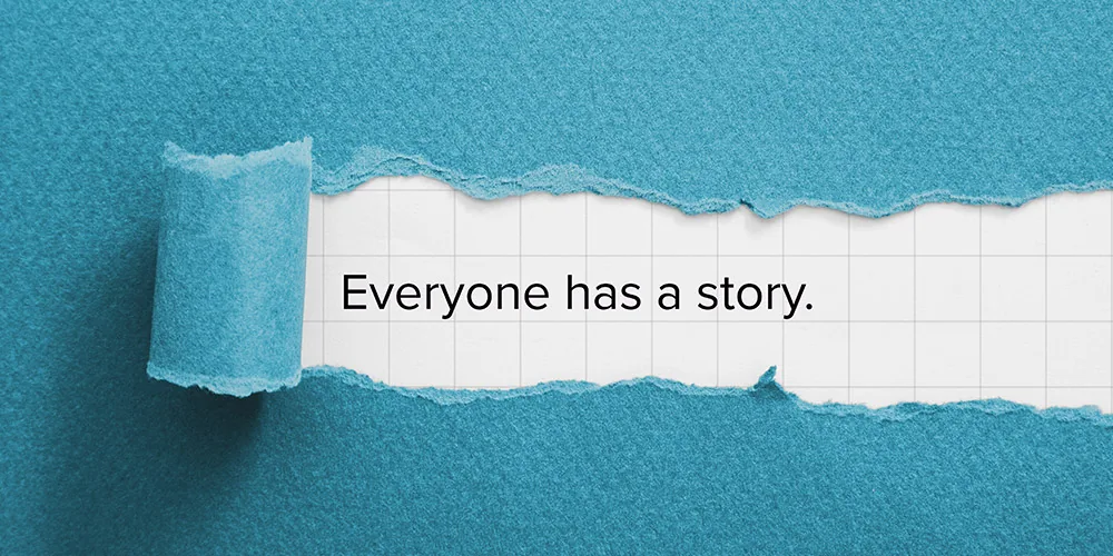 Torn blue paper revealing the words Everyone has a story printed on a grid-lined page underneath
