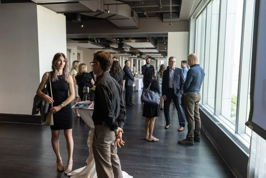 Attendees mingling at an office reception, standing in small groups along a window-lined hallway