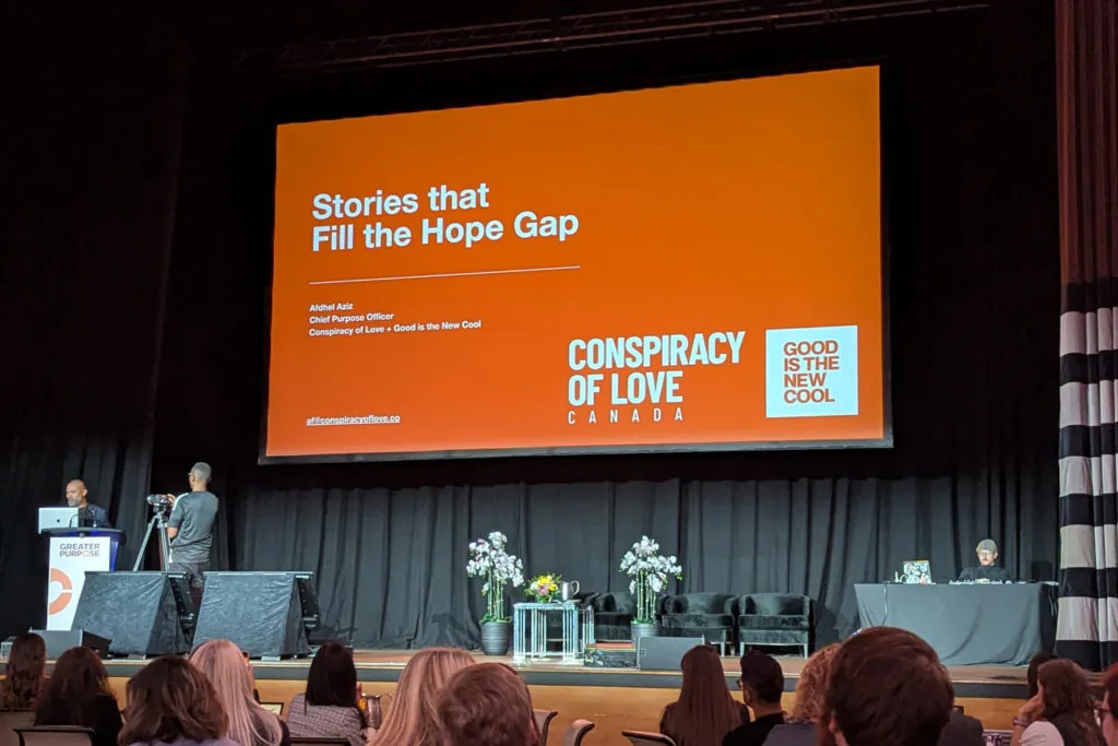 A conference stage screen reading Stories that Fill the Hope Gap, Conspiracy of Love Canada, above an audience