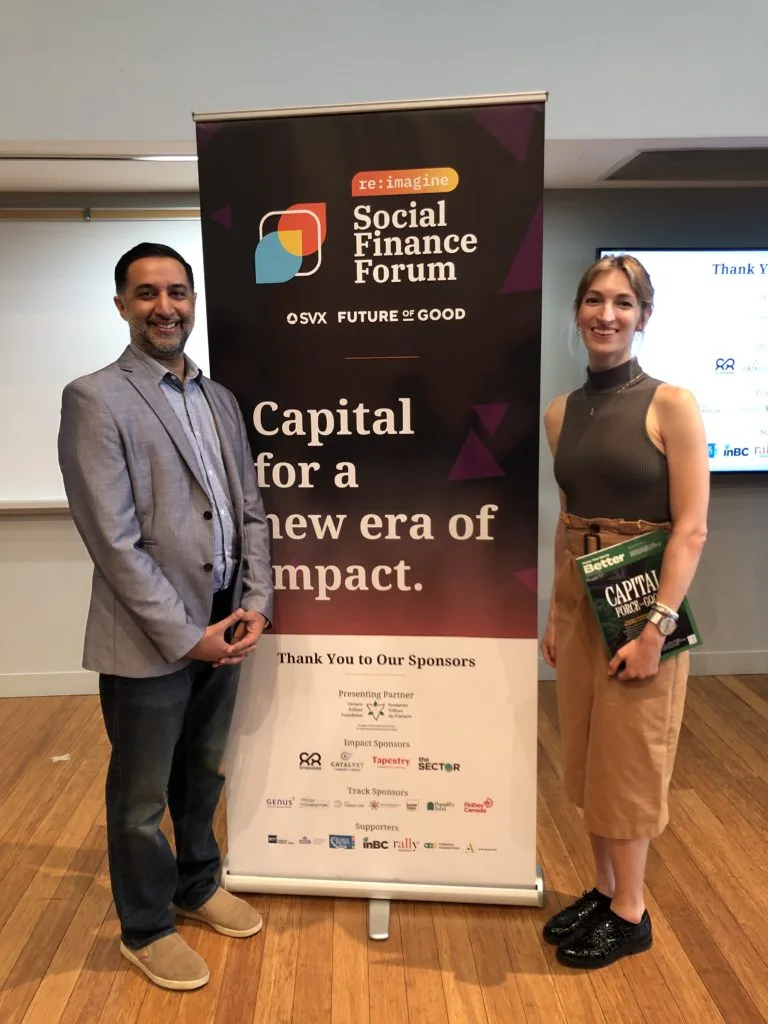 A man and woman posing beside a Social Finance Forum banner reading Capital for a New Era of Impact