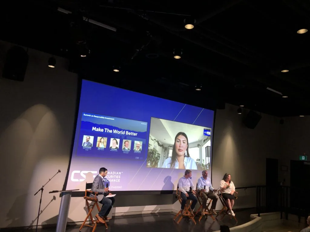 A moderator and panelists on stage below a screen reading Make The World Better with a video call guest