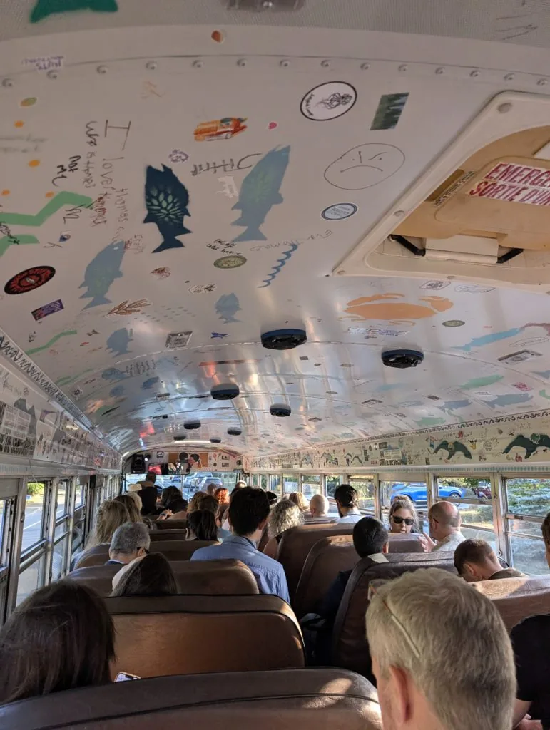 The decorated interior ceiling of a school bus covered in hand-drawn doodles, with passengers seated in the rows below